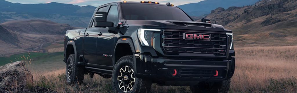 Black GMC pickup truck parked on a grassy hillside with mountains in the background at dusk